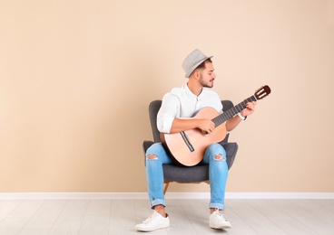 Photo of Handsome young man with guitar in armchair near color wall indoors. Space for text