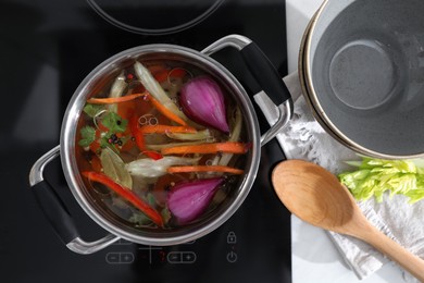 Photo of Kitchen counter with bowl, spoon and pot of delicious vegetable bouillon on stove, flat lay
