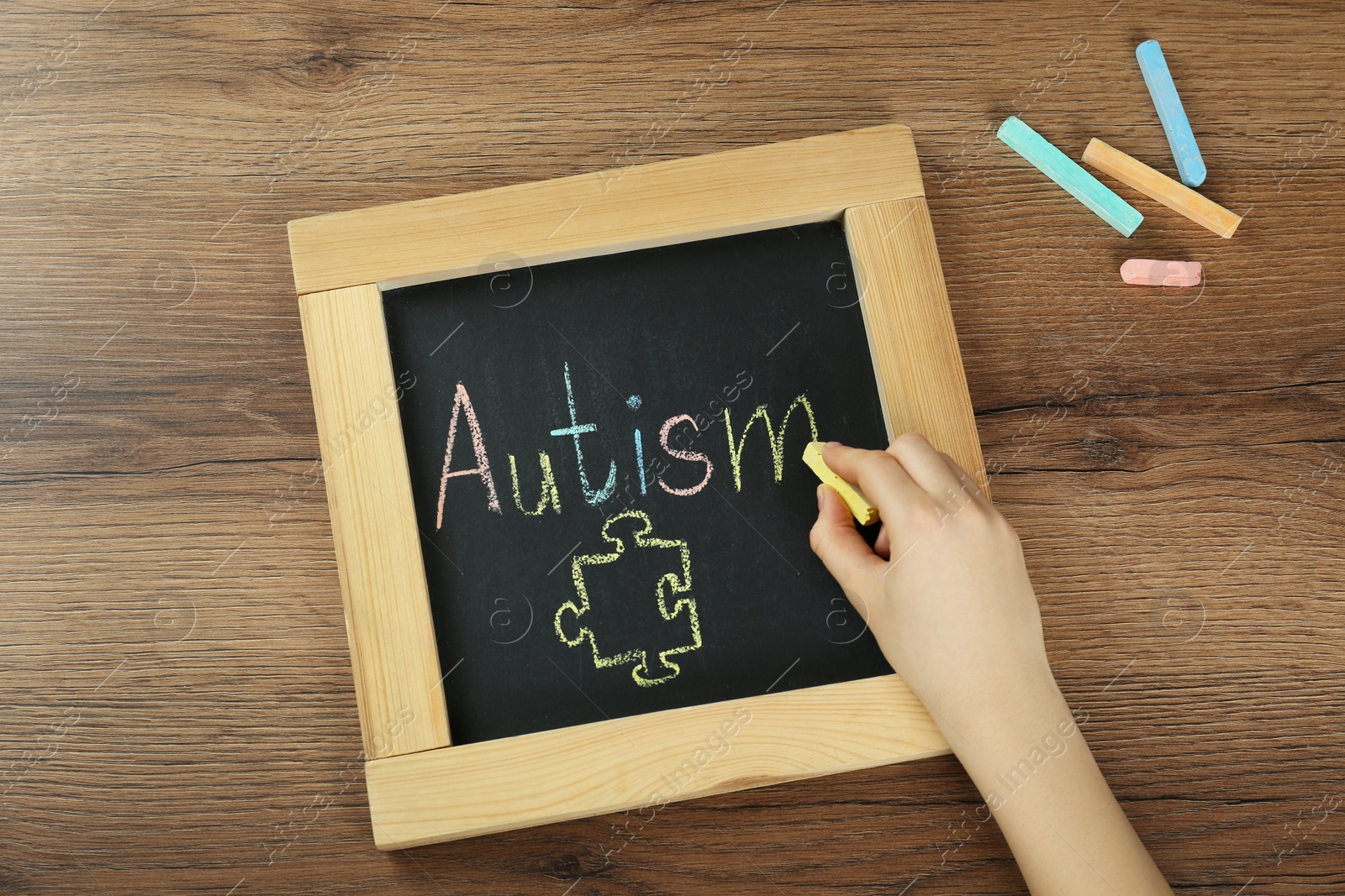 Photo of Woman writing word Autism on small blackboard with chalk at wooden table, top view