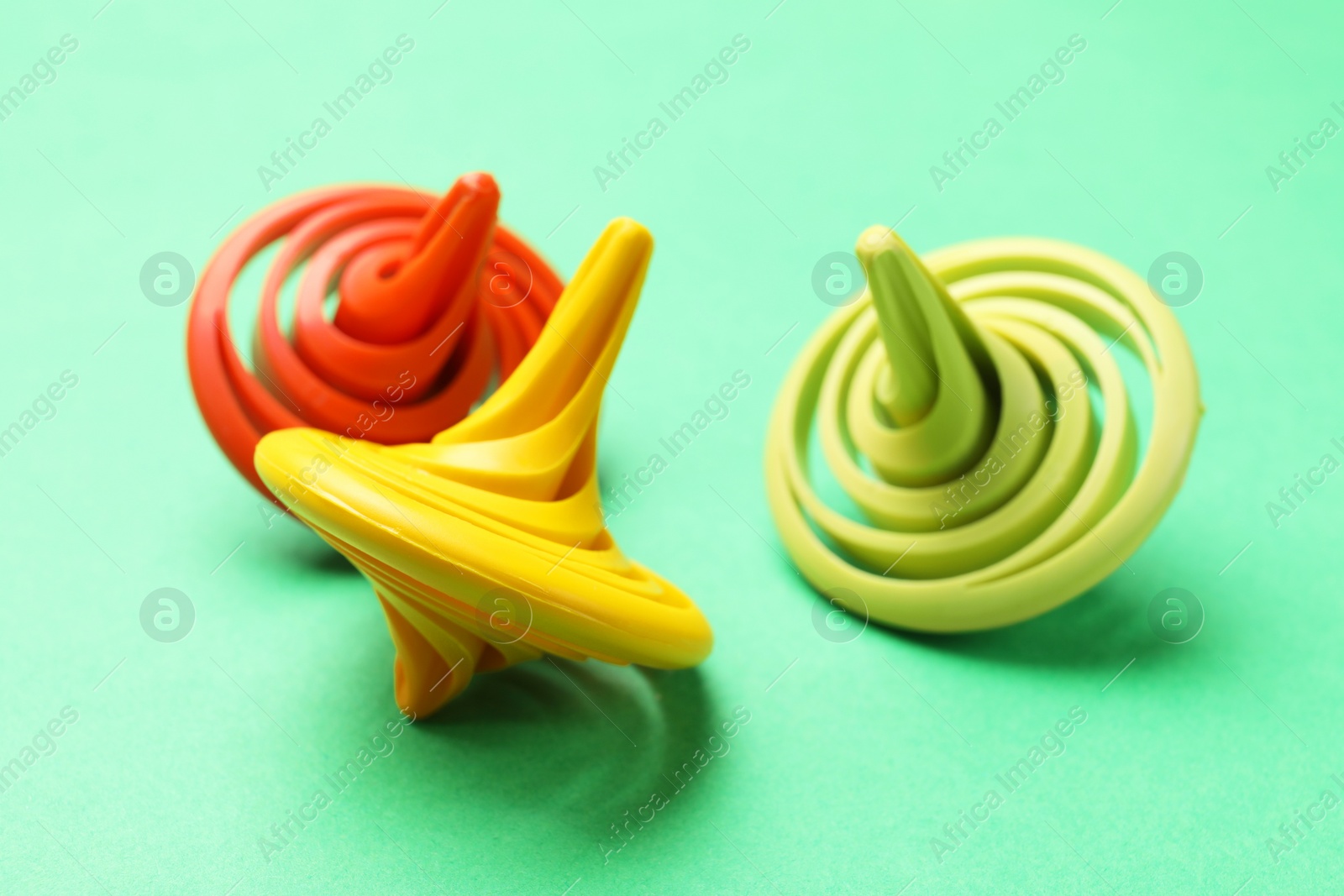 Photo of Many colorful spinning tops on green background, closeup