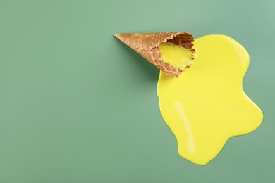 Photo of Melted ice cream and wafer cone on green background, above view. Space for text