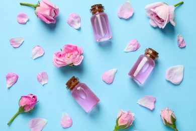 Photo of Fresh flowers, petals and bottles of rose essential oil on color background, flat lay