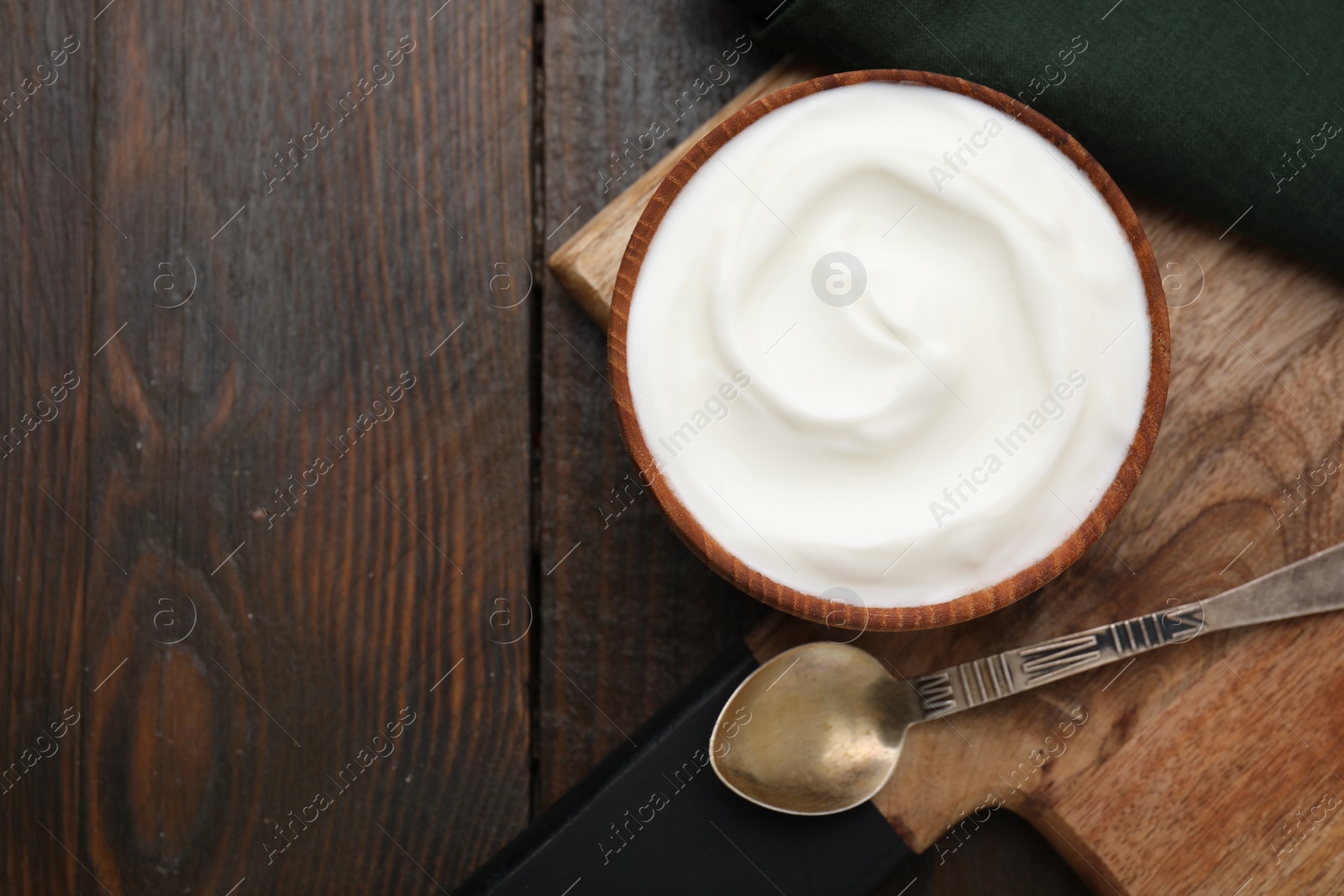 Photo of Delicious natural yogurt in bowl and spoon on wooden table, top view. Space for text