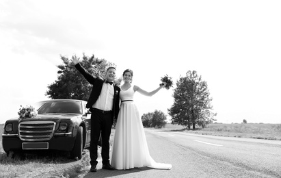 Photo of Happy bride and groom near car outdoors, black and white effect