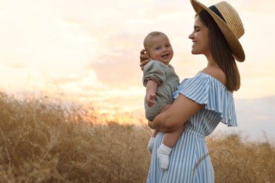 Happy mother with adorable baby in field at sunset, space for text