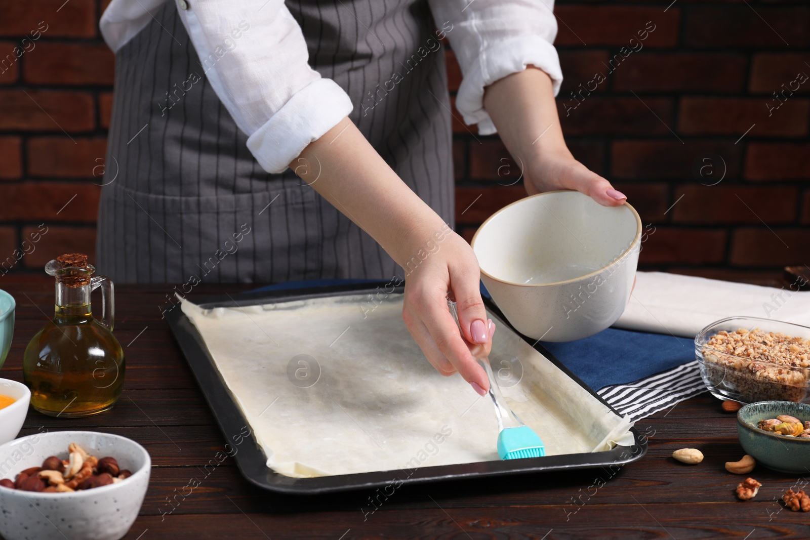 Photo of Making delicious baklava. Woman buttering dough in baking pan at wooden table, closeup