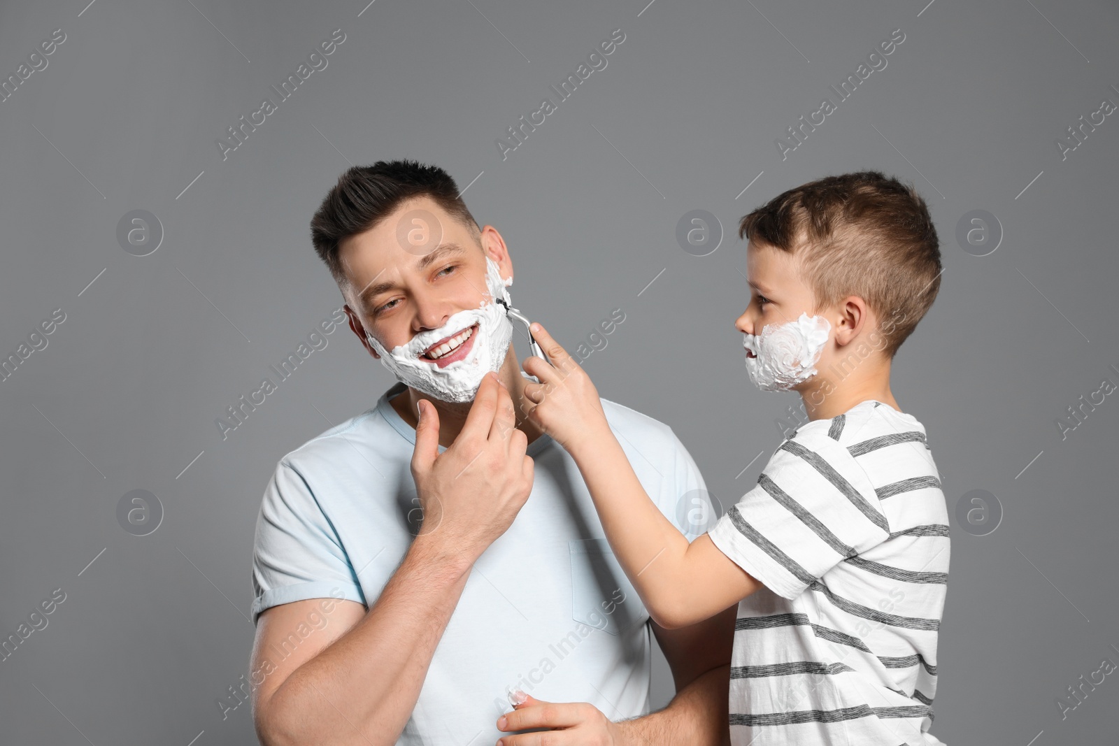 Photo of Son shaving his dad with razor on grey background