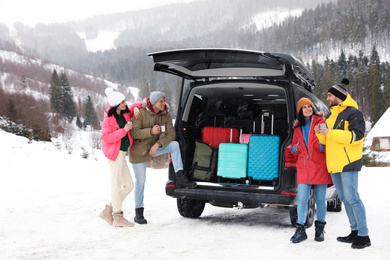 Photo of Group of friends near car with open trunk on snowy road. Winter vacation