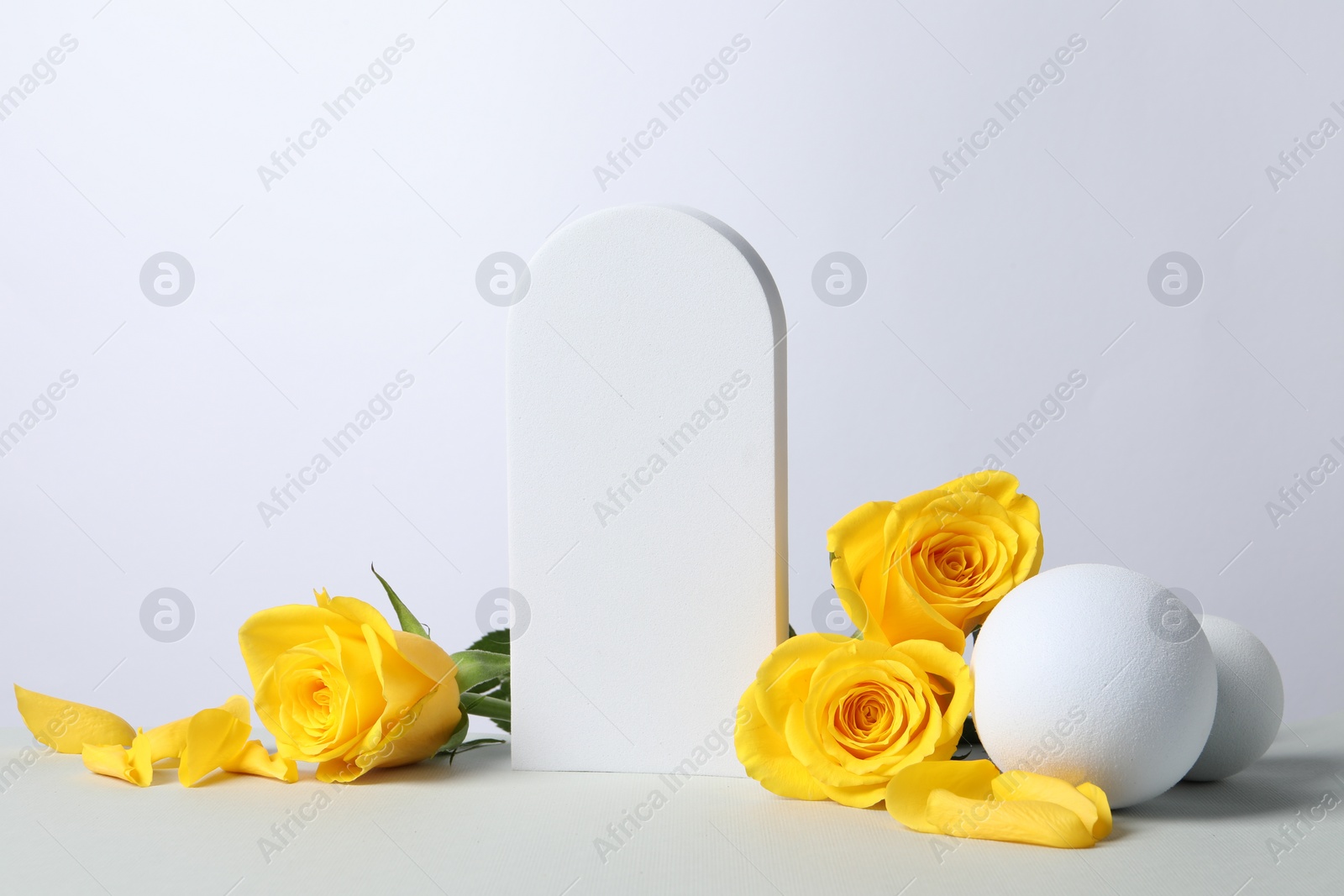 Photo of Beautiful presentation for product. Geometric figures and yellow roses on white table, space for text
