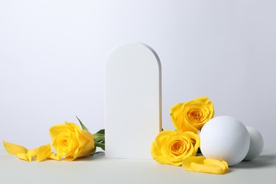 Photo of Beautiful presentation for product. Geometric figures and yellow roses on white table, space for text