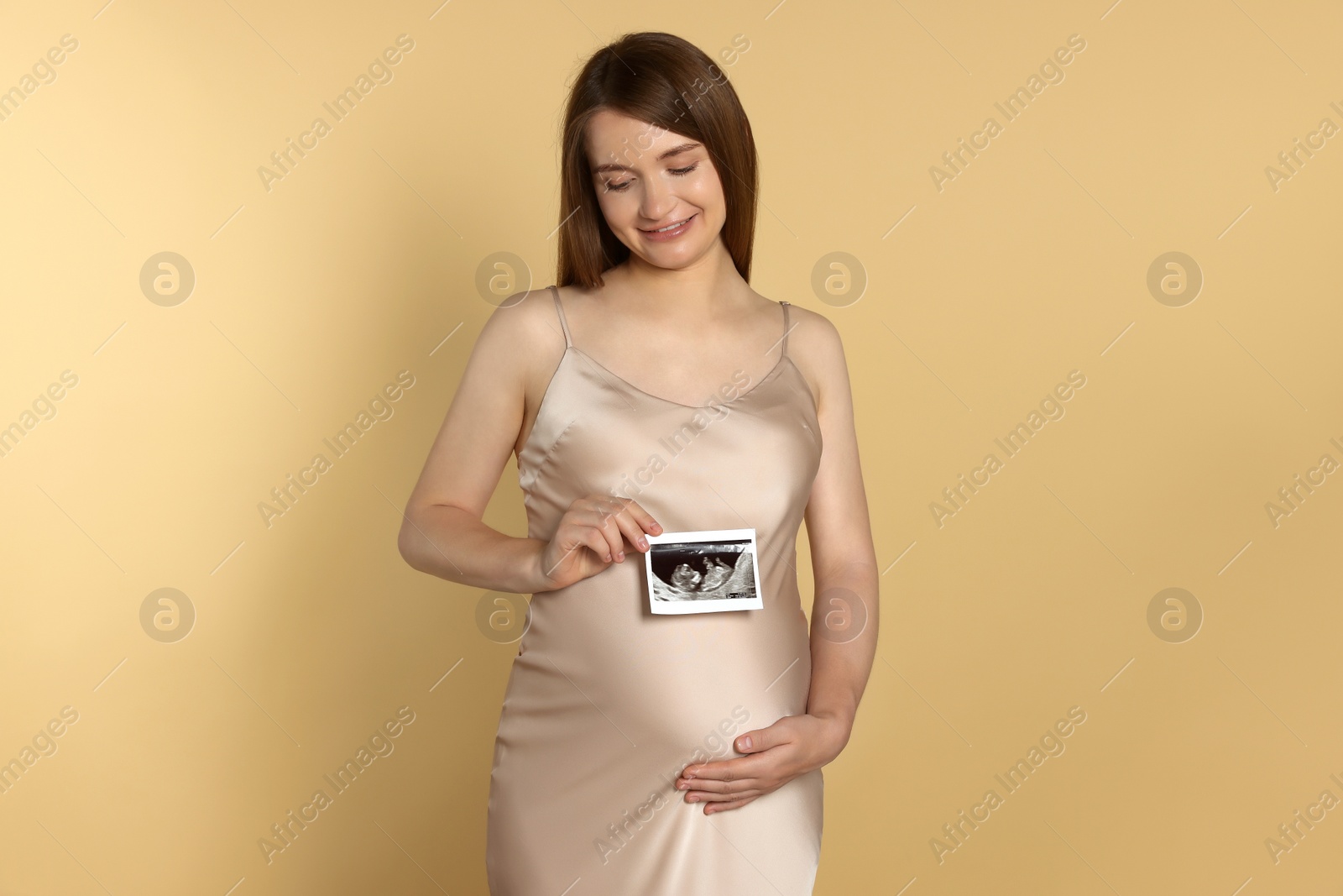 Photo of Pregnant woman with ultrasound picture of baby on beige background