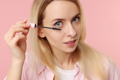 Photo of Beautiful woman applying mascara on pink background, closeup