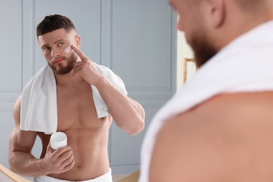 Photo of Handsome man applying cream onto his face near mirror in bathroom