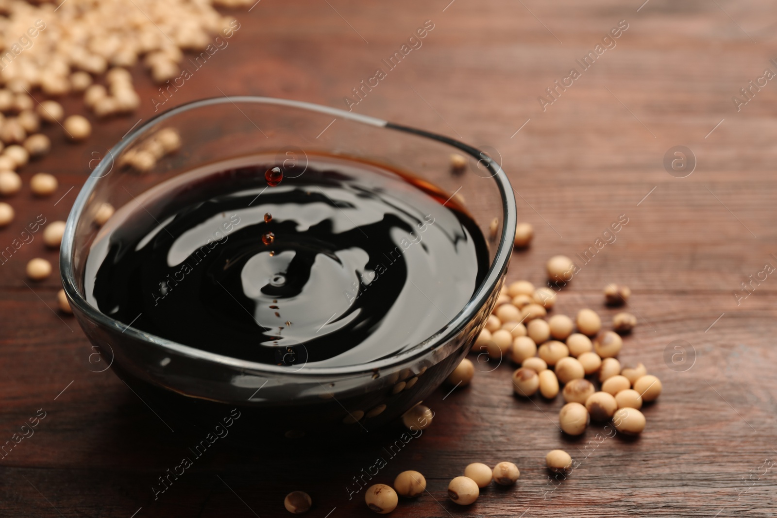 Photo of Soy sauce drops falling into bowl on wooden table, closeup. Space for text