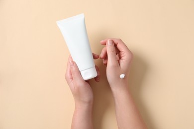 Woman with tube of hand cream on beige background, top view