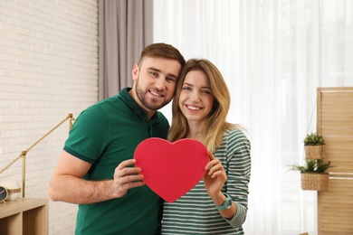 Happy young couple holding decorative heart indoors