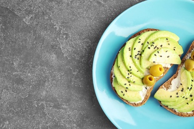 Crisp rye toasts with avocado, cream cheese and olives on plate, top view