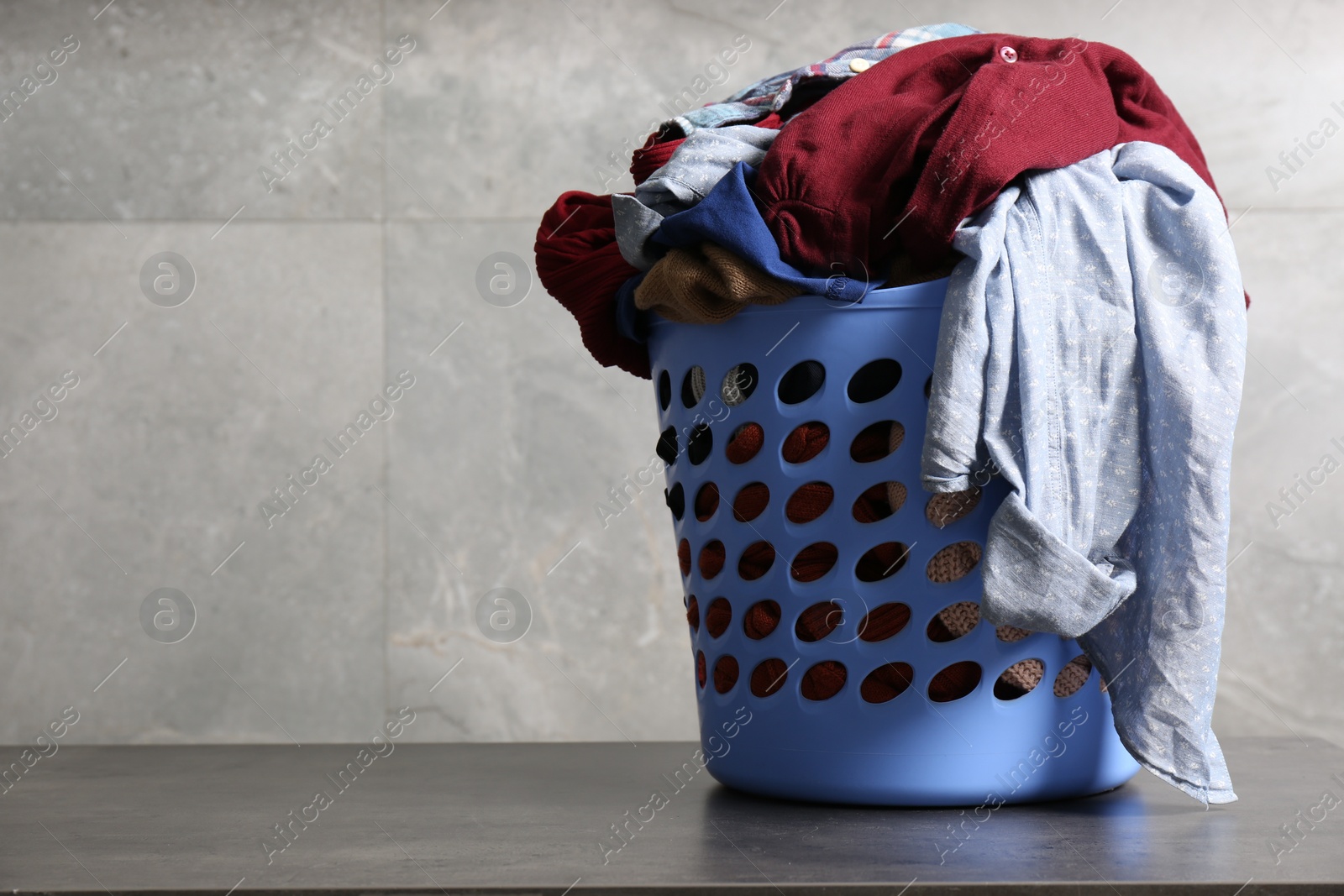 Photo of Laundry basket with clothes near grey wall. Space for text