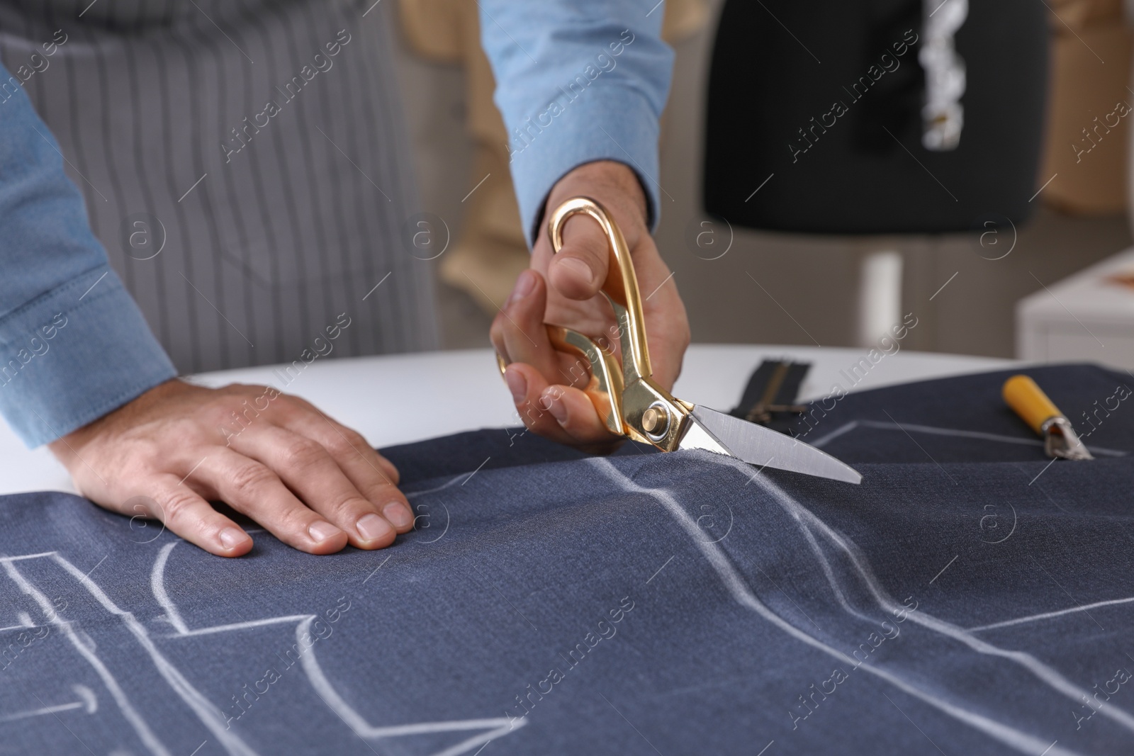 Photo of Tailor cutting fabric with scissors at table in atelier, closeup