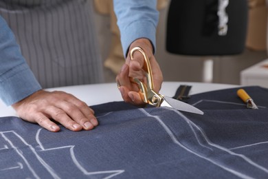 Tailor cutting fabric with scissors at table in atelier, closeup