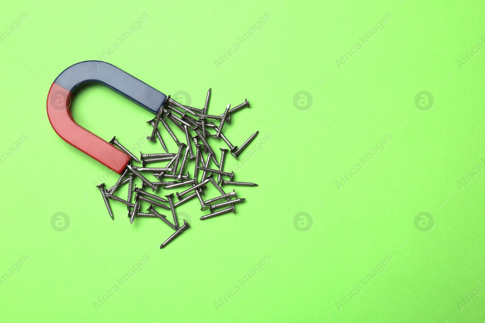 Photo of Magnet attracting nails on color background, top view with space for text