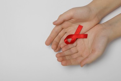 Little girl holding red ribbon on grey background, top view with space for text. AIDS disease awareness