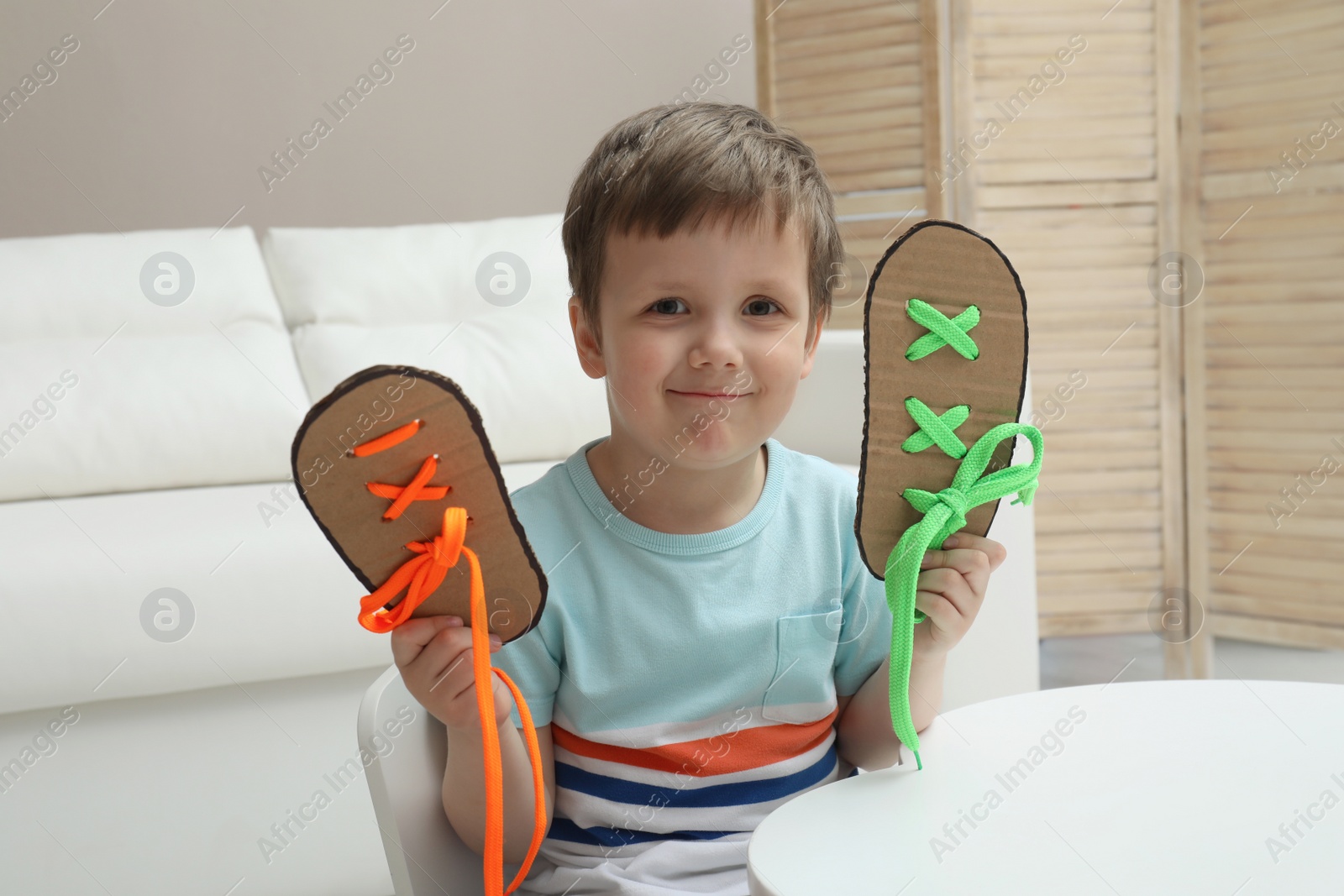 Photo of Cute little boy with shoe lacing cards at white table