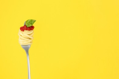 Fork with tasty pasta, tomato sauce and basil on yellow background, space for text