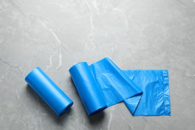 Rolls of light blue garbage bags on grey marble table, flat lay. Space for text