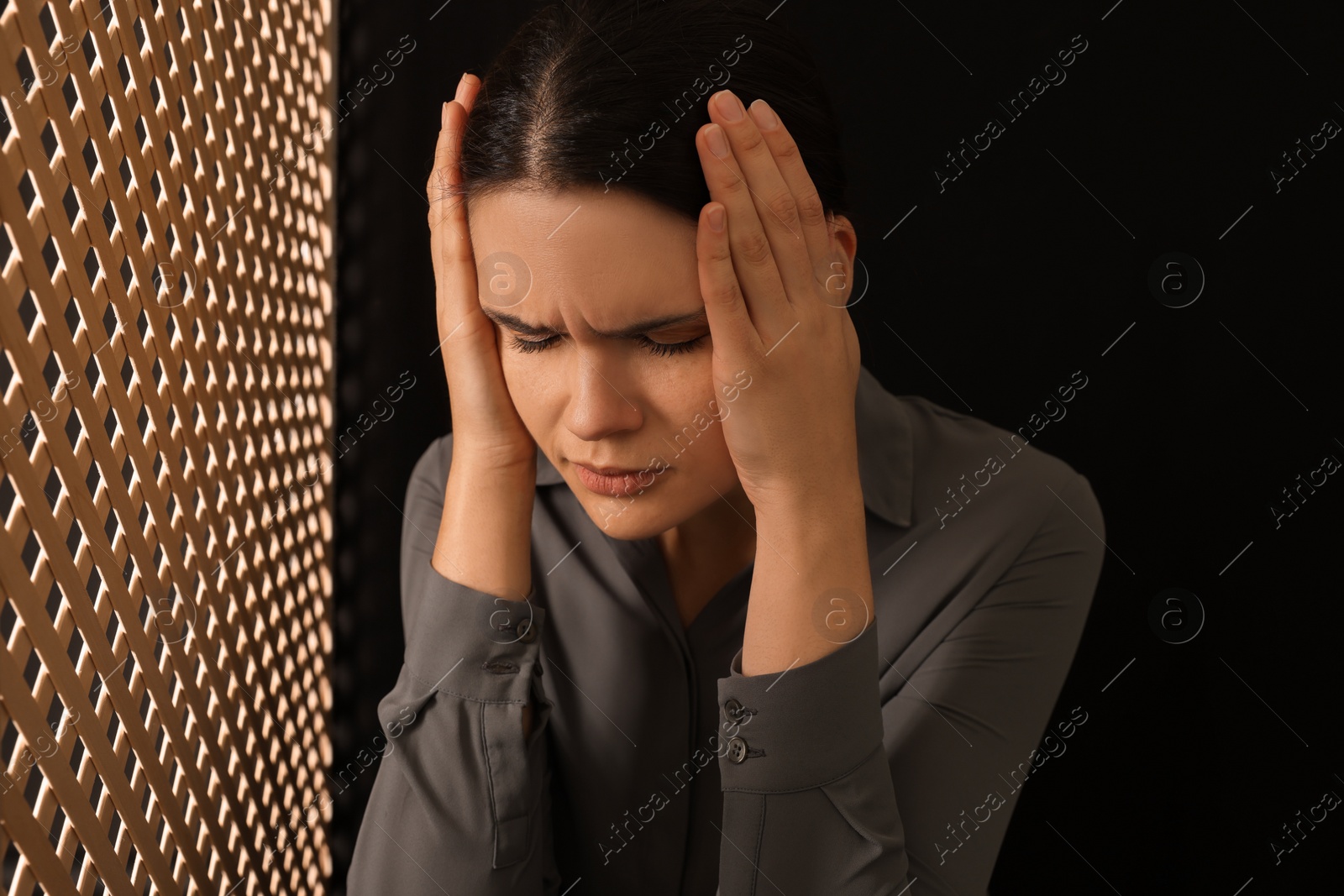 Photo of Repentant woman during confession near wooden partition in booth