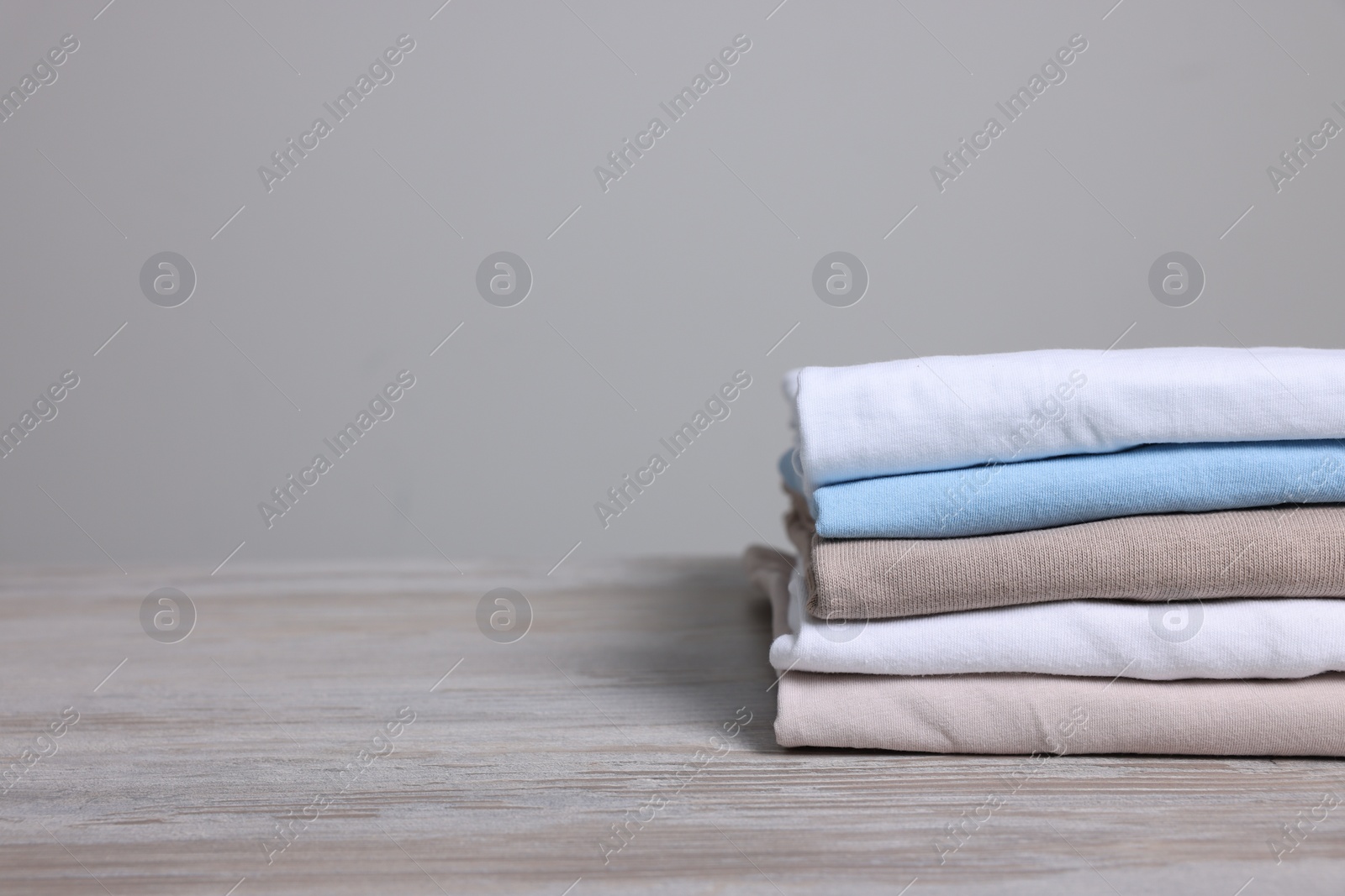 Photo of Sorting and organizing. Stack of different folded clothes on light wooden table, closeup. Space for text