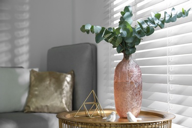 Beautiful eucalyptus branches and decor on stand near window, space for text. Interior element