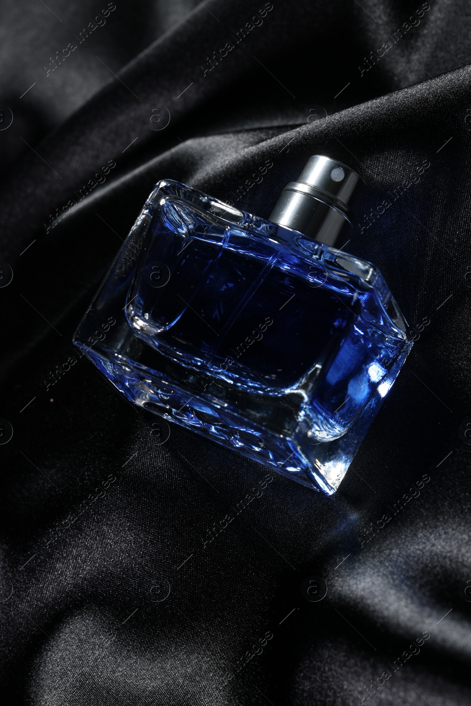 Photo of Luxury men's perfume in bottle on black satin fabric, above view