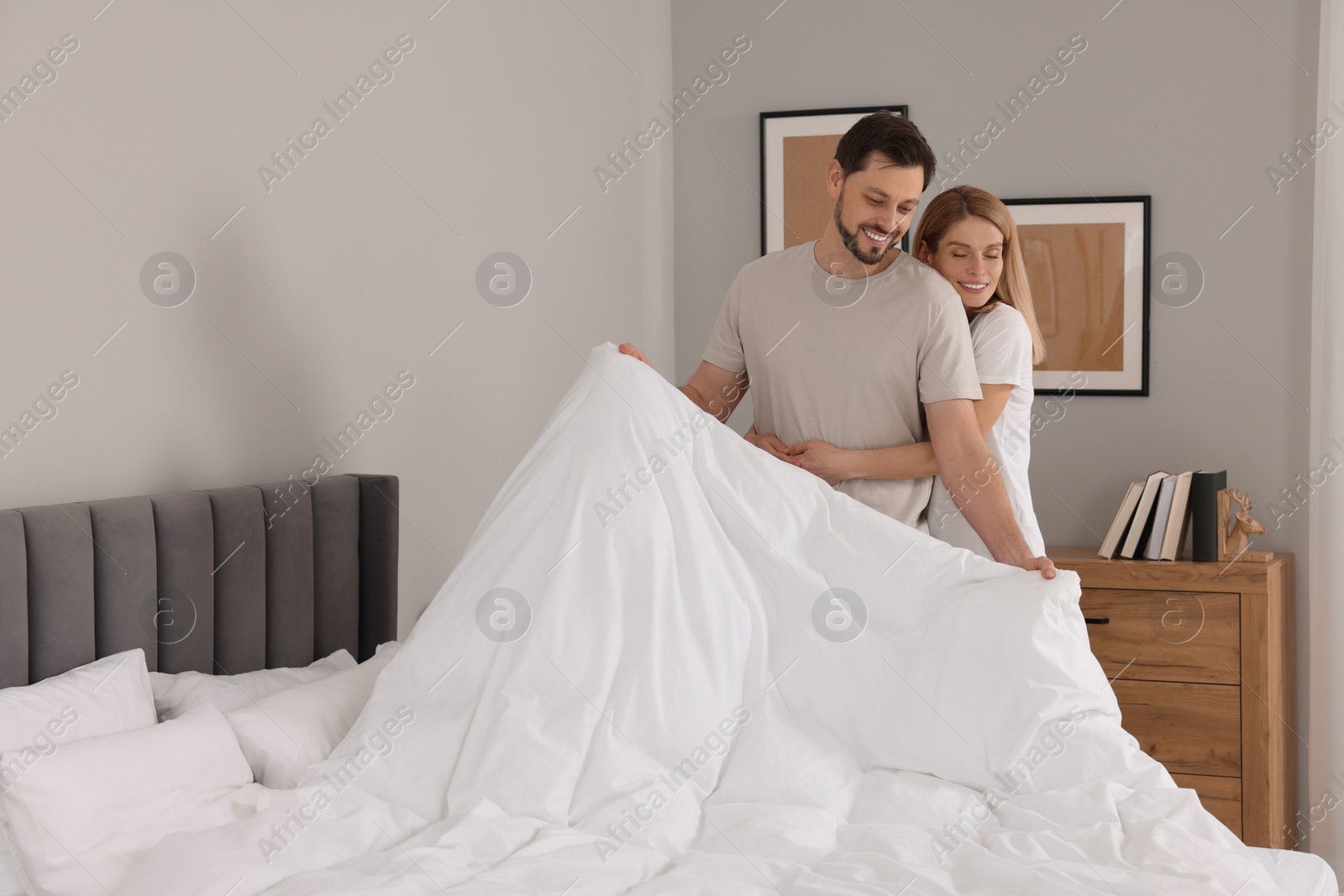 Photo of Couple changing bed linens in room. Space for text