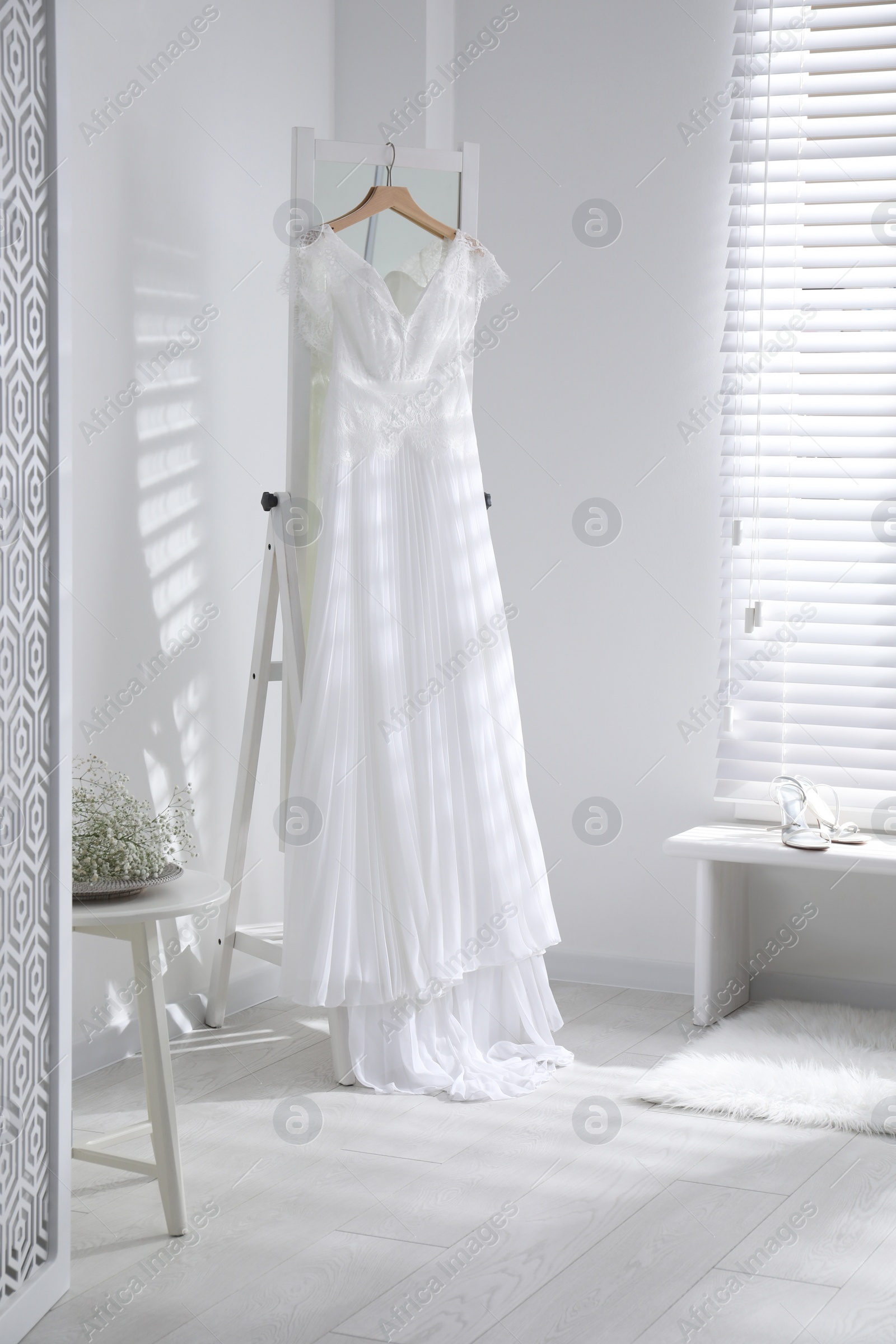 Photo of Beautiful wedding dress hanging on mirror in room