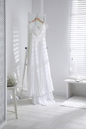 Photo of Beautiful wedding dress hanging on mirror in room