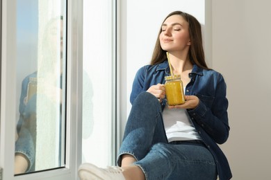 Beautiful young woman with delicious smoothie near window. Space for text