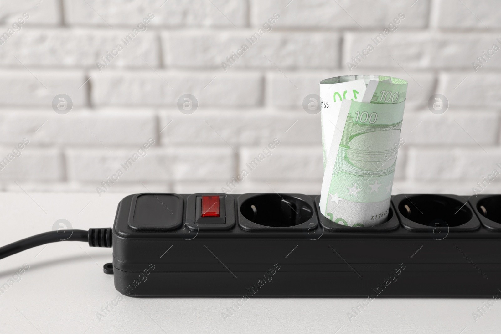 Photo of Extension board with rolled euro banknotes on white table near brick wall, closeup