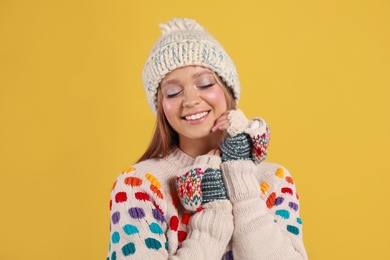 Photo of Young woman in warm sweater, mittens and hat on yellow background. Winter season