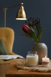 Vase with beautiful protea flowers and candles on wooden table indoors. Interior elements