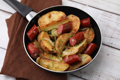 Photo of Fried potatoes with thin dry smoked sausages on white wooden table