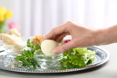 Photo of Woman holding traditional egg over Passover (Pesach) Seder plate on table, closeup