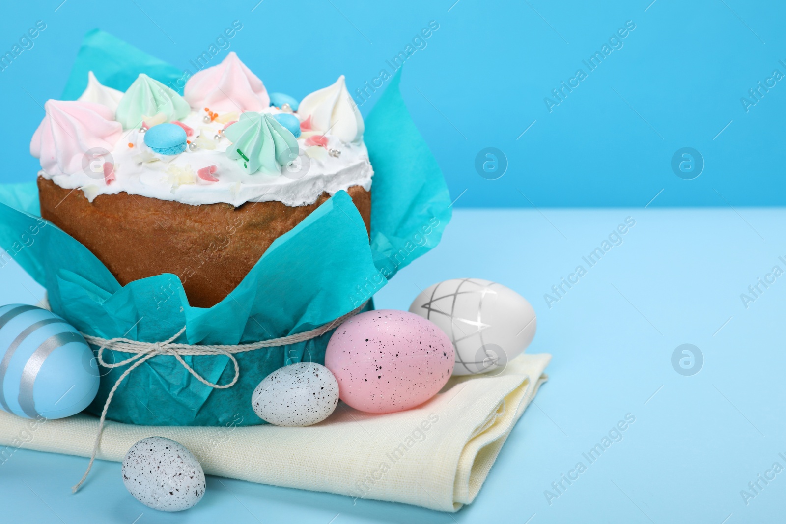 Photo of Traditional Easter cake with meringues and painted eggs on light blue background, space for text