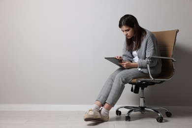 Photo of Young woman with bad posture using tablet while sitting on chair near grey wall. Space for text