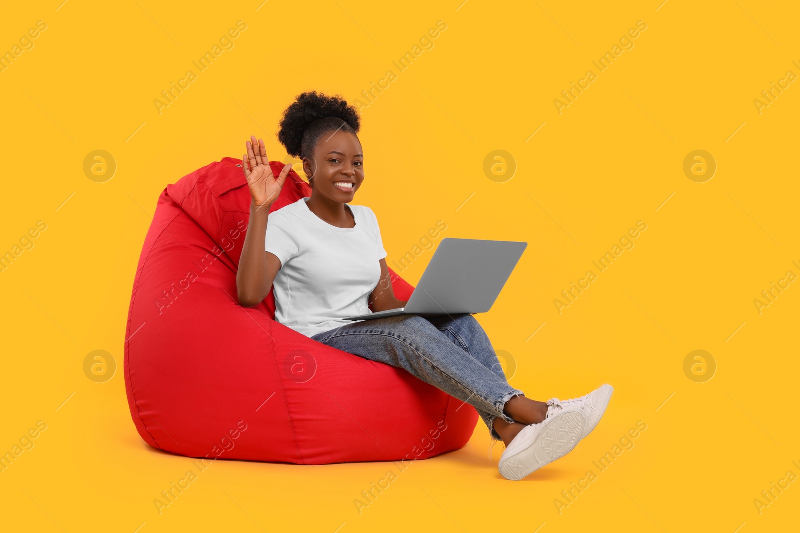 Photo of Beautiful young woman with laptop sitting on beanbag chair against orange background. Space for text