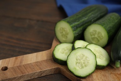 Photo of Fresh whole and cut cucumbers on wooden table, closeup