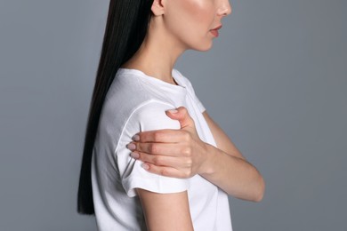 Photo of Woman suffering from shoulder pain on grey background, closeup