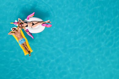 Happy couple with inflatable ring and mattress in swimming pool, top view. Summer vacation