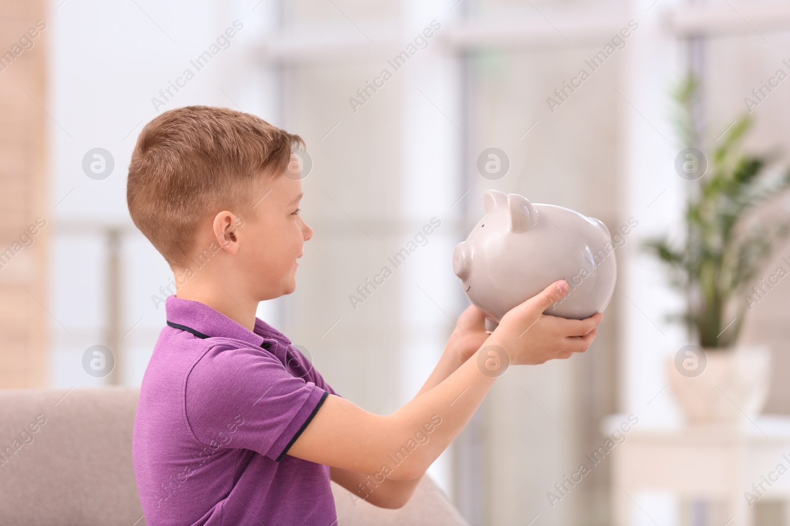 Photo of Little boy with piggy bank at home