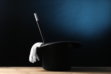 Photo of Magician's hat, gloves and wand on wooden table against dark background